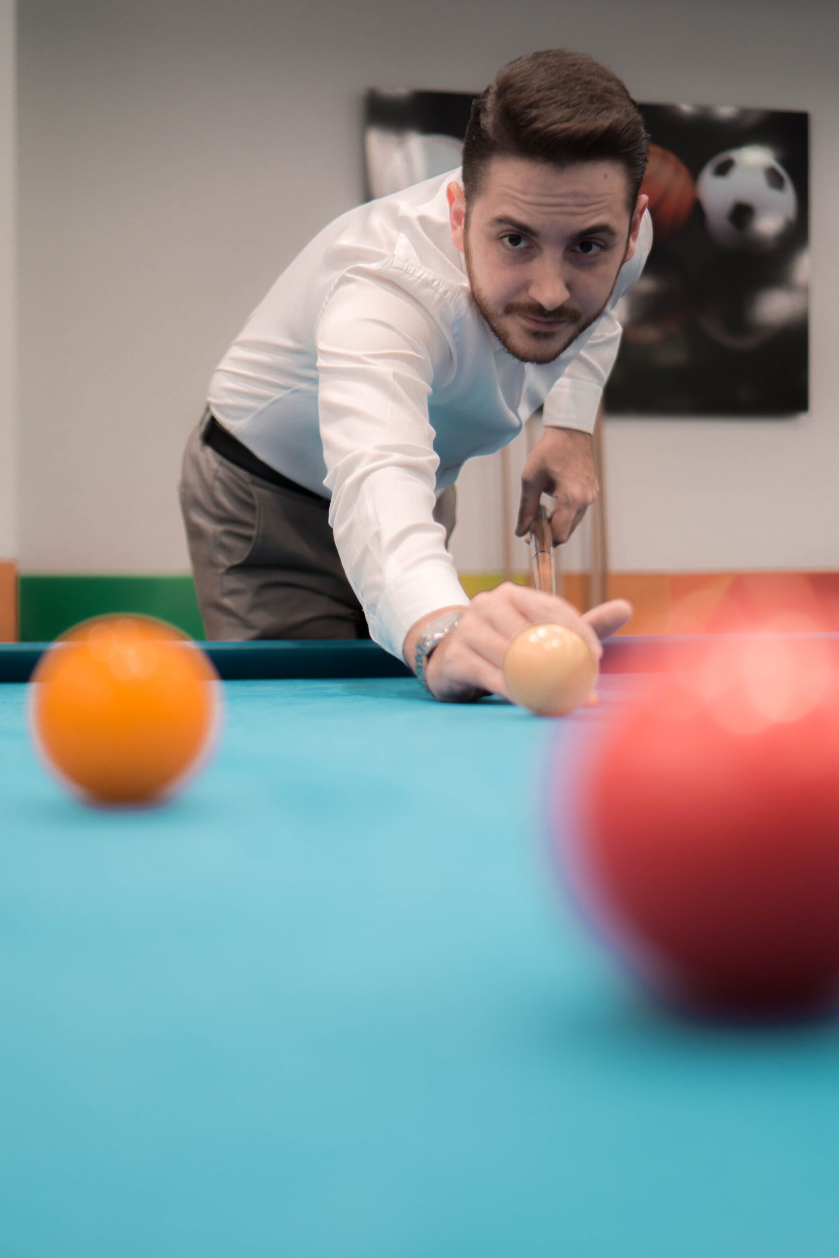 Man playing pool on a blue-felt table, aiming a cue at the billiard balls.